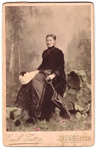 Fotografie Emil Tietze, Bad Elster, Portrait älterer Dame im samtenen Kleid mit Schirm und Haube in der Hand