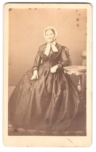 Fotografie unbekannter Fotograf und Ort, Portrait älterer Frau im seidenen reifrock Kleid mit Haube