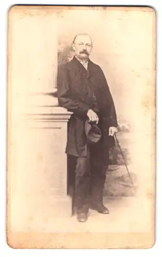 Fotografie A. Rossberg, Nossen, am Markt, Portrait Herr im Anzug mit Hut und Stock an einer Säule