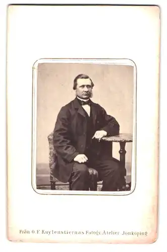 Fotografie O.F. Kuylenstiernas, Jönköping, Portrait Herr im Anzug mit Fliege sitzt am Tisch