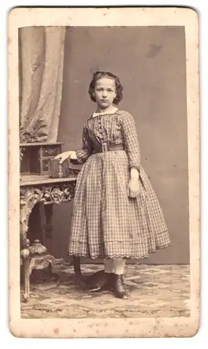 Fotografie M. Keller, Augsburg, Portrait niedliches Mädchen im karierten Kleid steht am Sekretär