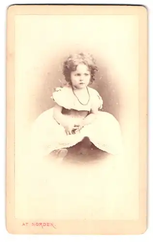 Fotografie At. Norden, Hamburg, Jungfernstieg 14, Portrait kleines Mädchen im weissen Kleid mit Perlenkette und Locken