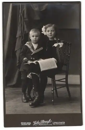 Fotografie Gebr. Strauss, Heidelberg, Hauptstrasse 88, Portrait junges Mädchen im Kleid und Junge mit Zeitung