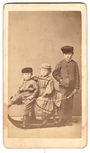 Fotografie M. Keller, Augsburg, Portrait Kinder in Anzügen und Kleid posieren auf einem Schlitten