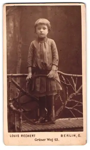 Fotografie Louis Rechert, Berlin, Grüner Weg 63, Portrait niedliches Mädchen im Kleid mit Reifen am Holzzaun stehend