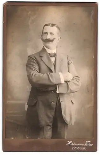 Fotografie Hartmann Frères, Vic-sur-Seille, Portrait eleganter Herr mit Schnauzbart und verschränkten Armen