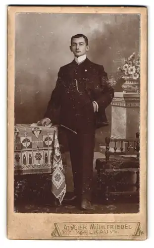Fotografie Mühlfriedel, Wilkau i. S., Portrait junger Mann im feinen Anzug stehend am Tisch