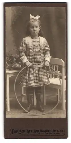 Fotografie Pariser Atelier, Mannheim S. 1. 4., Breitestrasse, Portrait kleines Mädchen im karierten Kleid mit Reifen
