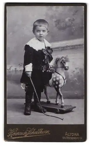 Fotografie Heinrich Schellhorn, Altona, Gr. Roonstr. 73, Portrait kleiner Knabe im Samtkleid mit Schaukelpferd und Gerte