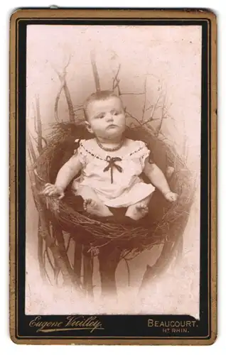 Fotografie Eugene Vuillep, Beaucourt, Portrait Kleinkind im Kleidchen mit Perlenkette sitzt in einem Nest