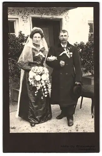 Fotografie Gg. Röckenwagner, Grafing-Markt, Ehepaar im schwarzen Kleid und Mantel mit Orden