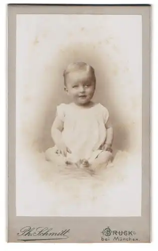 Fotografie Ph. Schmitt, Bruck bei München, Portrait süsses blondes Kleinkind im weissen Hemdchen auf Fell sitzend