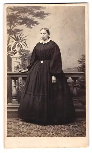 Fotografie unbekannter Fotograf und Ort, Portrait Dame im dunklen reifrock Kleid vor einer Studiokulisse