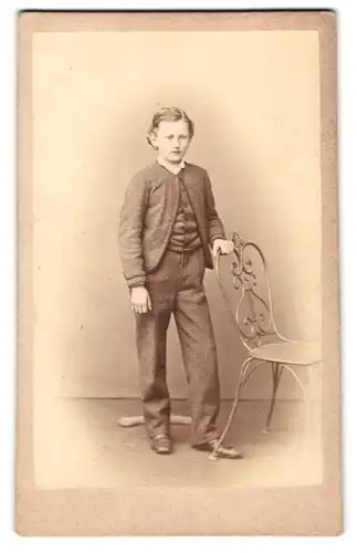 Fotografie Kauffmann & Kessler, Bad Kreuznach, hinter d. Kurhaus, Portrait junger Knabe im grauen Anzug am Stuhl stehend