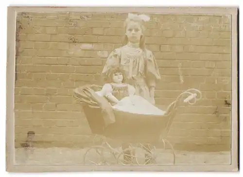 Fotografie unbekannter Fotograf und Ort, Mädchen im Kleid mit grosser Puppe im Kinderwagen