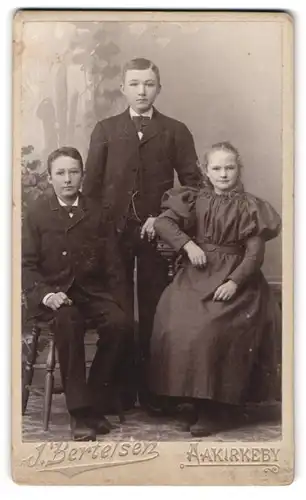 Fotografie J. Bertelsen, Aakirkeby, Junges Mädchen in Kleid mit Puffärmeln mit Brüdern in Anzügen