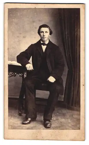 Fotografie J. Hansens, Nexö, Portrait junger Mann im dunklen Anzug mit Fliege sitzend im Atelier