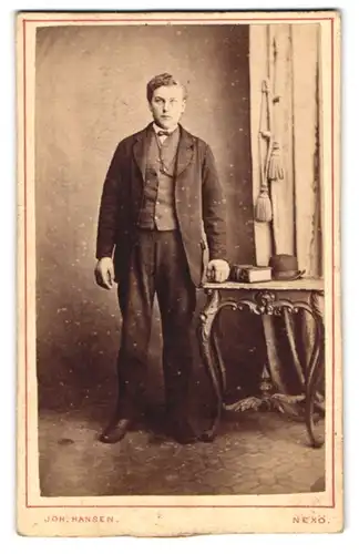 Fotografie Joh. Hansen, Nexö, Portrait junger Mann C. Jensen im Anzug mit auf Tisch liegender Melone