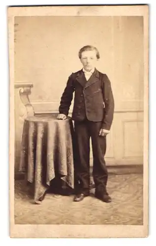Fotografie A. Stöckel, Rönne, Portrait junger Knabe im feinen Anzug stehend am Tisch