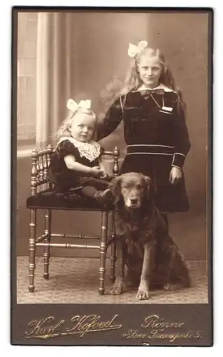 Fotografie Karl Kofoed, Rönne, Portrait zwei blonde Mädchen in Samtkleidern mit schwarzem Hund zu Füssen