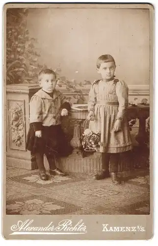 Fotografie Alexander Richter, Kamenz i. S., Portrait zwei kleine Kinder in Kleidern mit Blumenkorb, Schielend