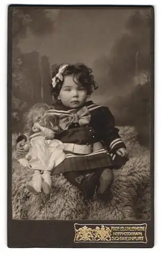 Fotografie Prof. Ed. Uhlenhuth, Schweinfurt, Portrait kleines Mädchen mit grosser Puppe sitzt auf einem Fell
