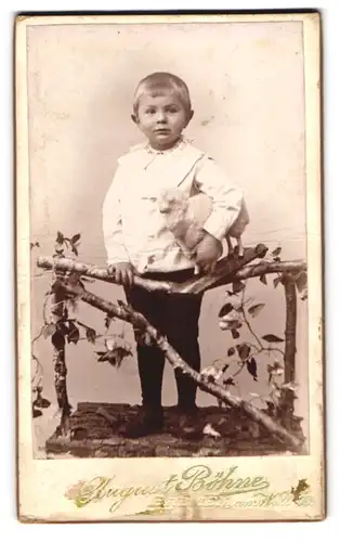 Fotografie August Böhne, Bremen, am Wall 78, Portrait junger Knabe in weisser Bluse mit Spielzeug Schaf im Arm