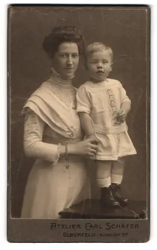 Fotografie Atelier Carl Schäfer, Elberfeld, Kipdorf 57, Portrait Mutter im hellen Kleid mit Sohn im Kleid, Mutterglück