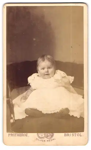 Fotografie Protheroe, Bristol, 36 Wine St., Portrait lächelndes Baby im weissen Taufkleidchen