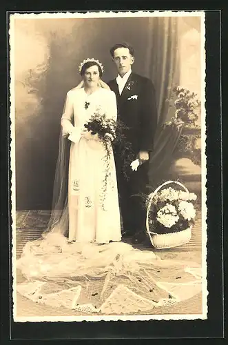 AK Hochzeit, Ehepaar, in festlichen Kleidern im Salon gesehen mit einem Korb voller Blumen daneben
