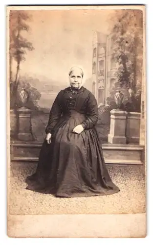 Fotografie unbekannter Fotograf und Ort, Portrait ältere Dame im Biedermeierkleid mit Haube vor einer Studiokulisse