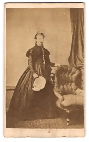 Fotografie unbekannter Fotograf und Ort, Portrait junge Frau im schwarzen reifrock Kleid mit Hut in der Hand