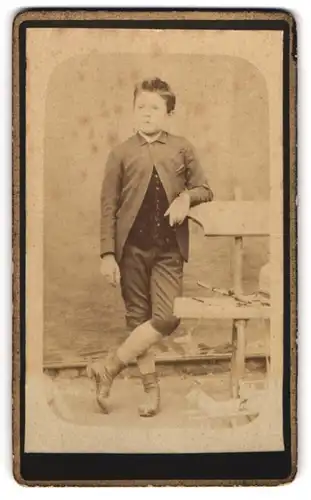 Fotografie unbekannter Fotograf und Ort, Portrait junger Knabe in kurzen Hosen lehnt lässig an einer Bank