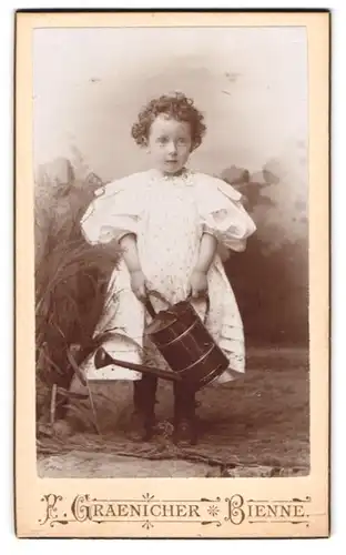 Fotografie Graenicher, Bienne, 60, Parsquart Promenade, Portrait kleines Mädchen im Kleid mit Giesskanne