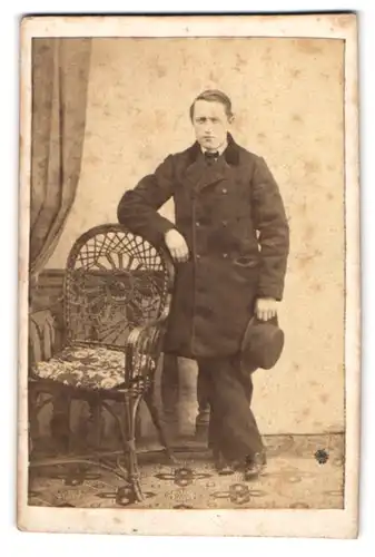Fotografie unbekannter Fotograf und Ort, Portrait junger Mann im Mantel mit Hut in der Hand