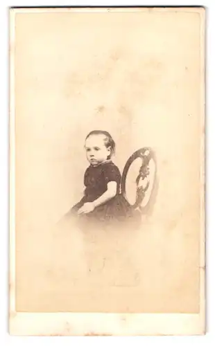Fotografie J. F. Long, Exeter, Portrait niedliches Mädchen im dunklen Kleid sitzt auf einem Stuhl