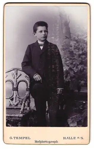 Fotografie G. Tempel, Halle a. S., Portrait junger Knabe im Anzug mit karierter Fliege und Hut in der Hand