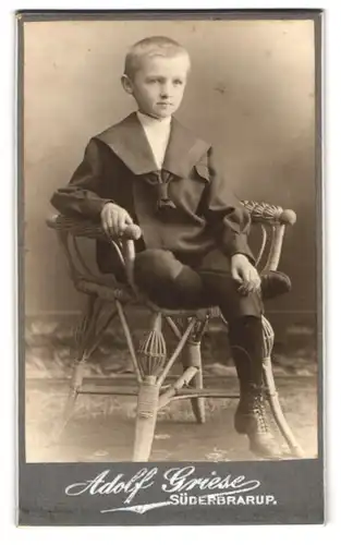 Fotografie Adolf Griese, Süderbrarup, Kleiner Junge mit Matrosenkragen sitzt lässig auf Korbstuhl