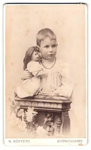 Fotografie W. Höffert, Hamburg, Jungfernstieg 12, Portrait kleiner Knabe mit seiner Puppe und Perlenkette im Atelier