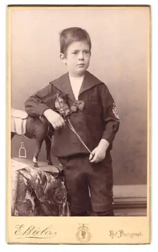 Fotografie E. Bieber, Berlin, Leipzigerstr. 128, Portrait junger Knabe im Matrosen Anzug mit Spielzeug Pferd