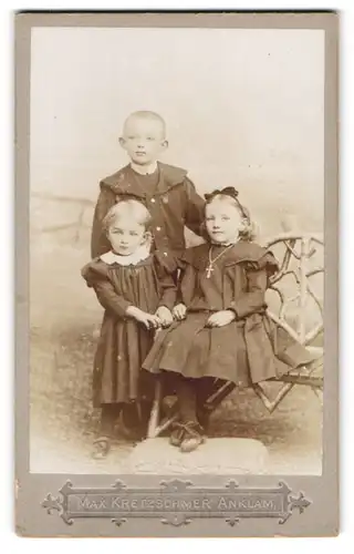 Fotografie Max Kretzschmer, Anklam, Portrait drei niedliche Kinder in Kleidern und Anzug mit Haarschleife