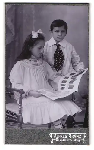 Fotografie Alfred Gränz, Stollberg i. Erzg., Portrait zwei Kinder im weissen Kleid und Hemd betrachten ein Fotoalbum