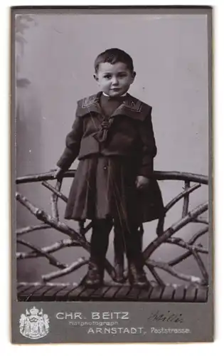 Fotografie Chr. Beitz, Arnstadt, Poststr., Portrait kleines Kind im dunklen Kleid steht auf einer Bank