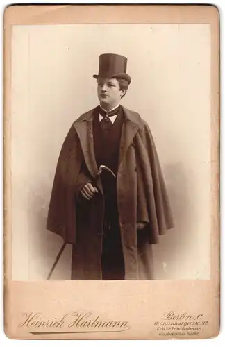 Fotografie Heinrich Hartmann, Berlin, Oranienburgerstr. 92, junger Mann im Anzug mit Mantel und Spazierstock, Zylinder