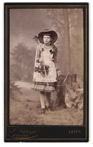 Fotografie Julius Schlegel, Leipa i. Böhm., Klostergasse 24, Portrait Mädchen als Gärtnerin im Kleid mit Harke