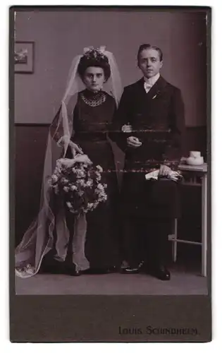 Fotografie Louis Schindhelm, Ebersbach i. S., Portrait junges Ehepaar im schwarzen Kleid und Anzug mit Zylinder