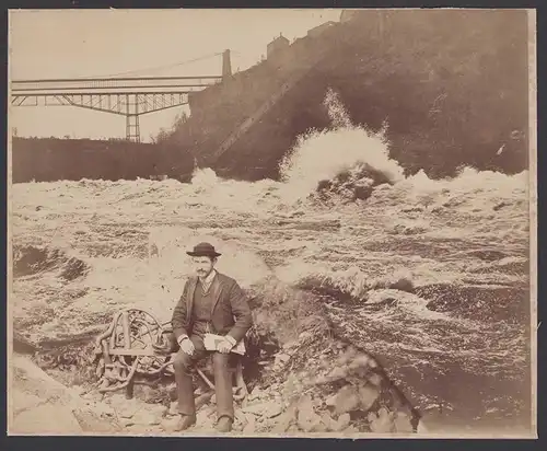Fotografie Fotomontage Wanderer auf Bank neben Wildwasser sitzend, Eisenbahnbrücke im Hintergrund