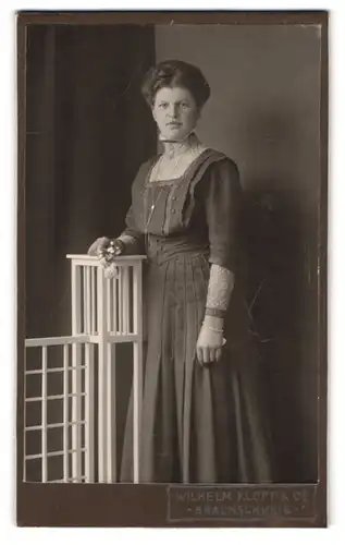 Fotografie Wilhelm Klopp, Braunschweig, Portrait dunkelhaarige Schönheit im bestickten Kleid und Blume in der Hand