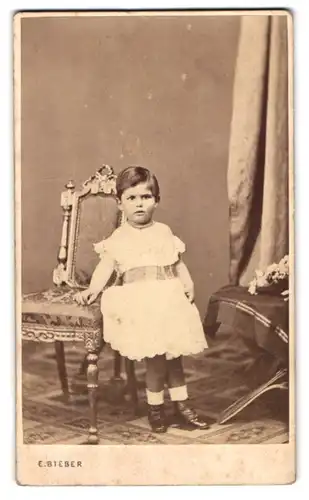 Fotografie E. Bieber, Hamburg, Gr. Bäckerstr. 26, Portrait kleines Mädchen im weissen Kleid neben einem Stuhl