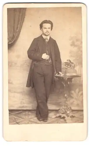 Fotografie unbekannter Fotograf und Ort, Portrait junger Mann im dunklen Anzug mit Schlips und Melone auf dem Tisch